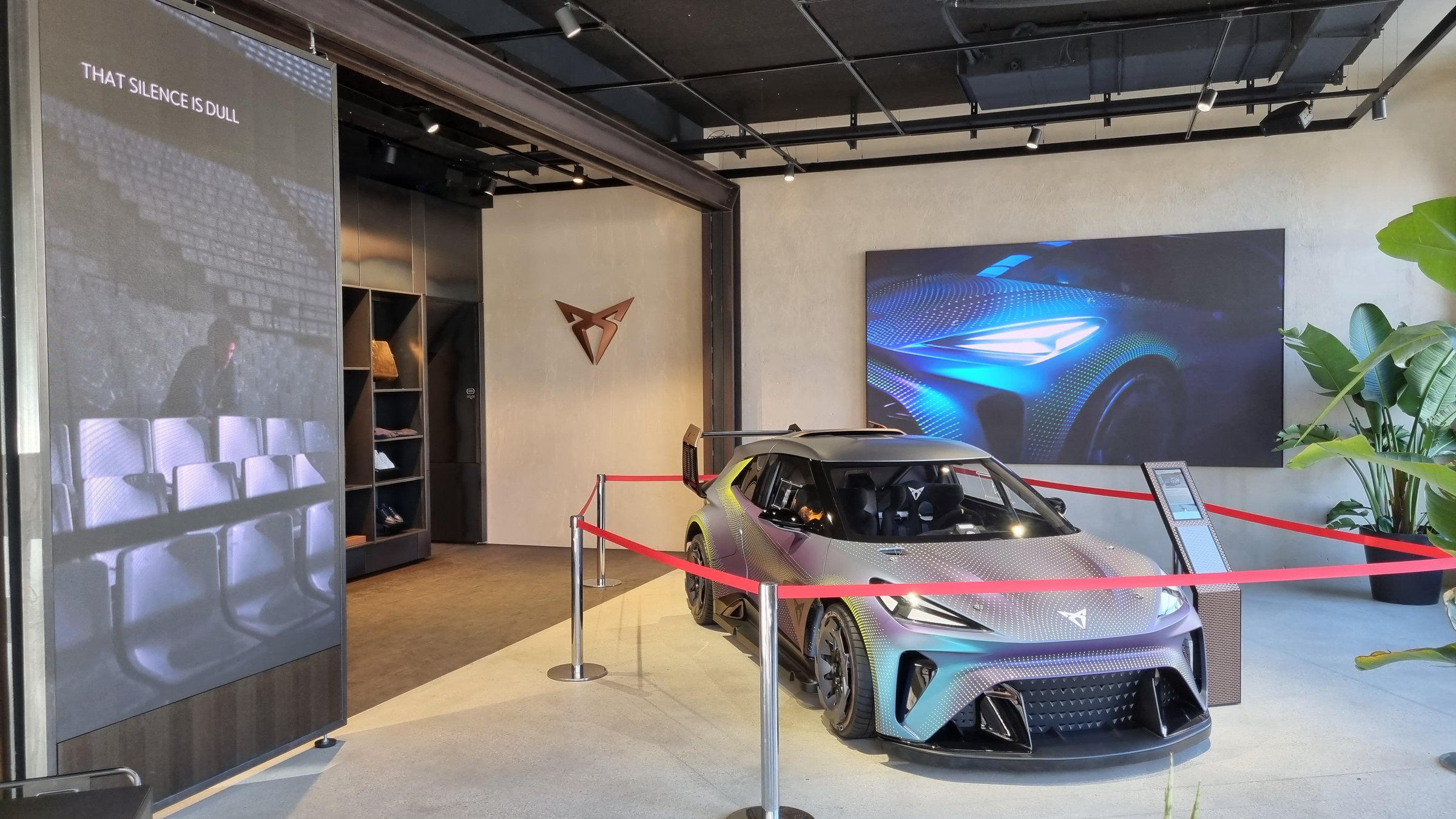 A car on show in a showroom, with a large wall screen behind it playing a film of a car