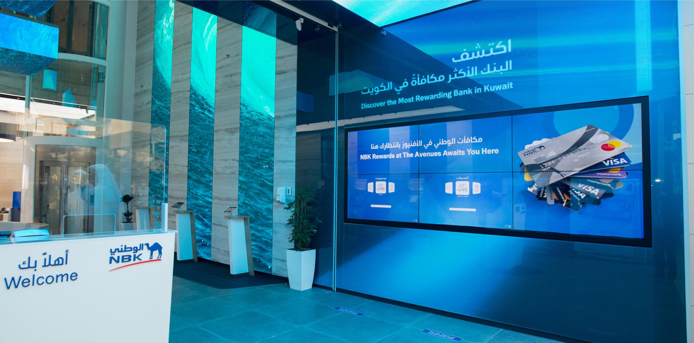 A video wall of six screens showing a rewards card offer, below the bank's slogan on a large screen, in a bank branch