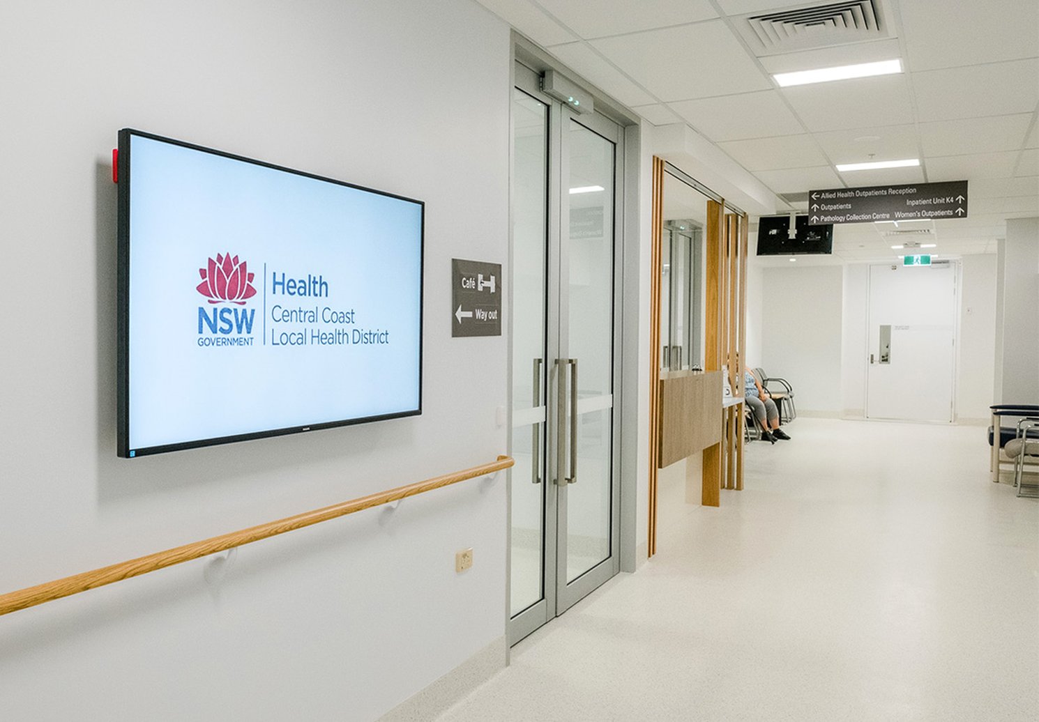 A wall screen showing the health service's name in a hospital corridor, beside the way to the outpatient clinics
