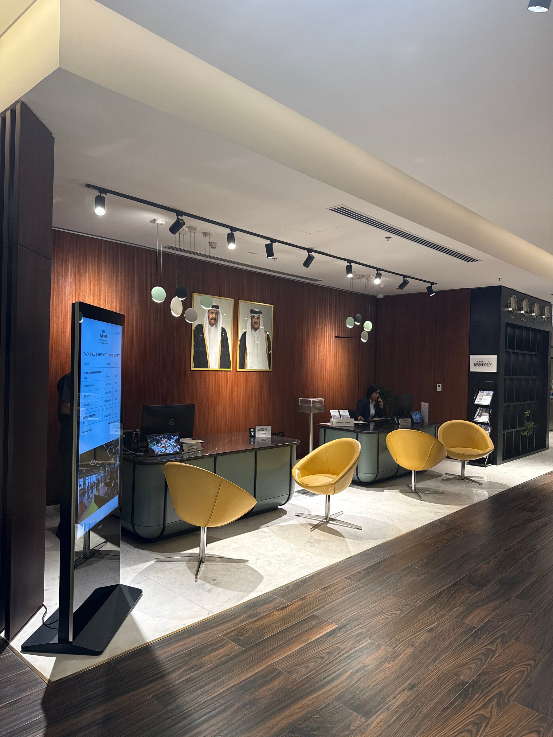 A standing screen listing the hotel's facilities and their hours, beside the reception desk of a hotel lobby