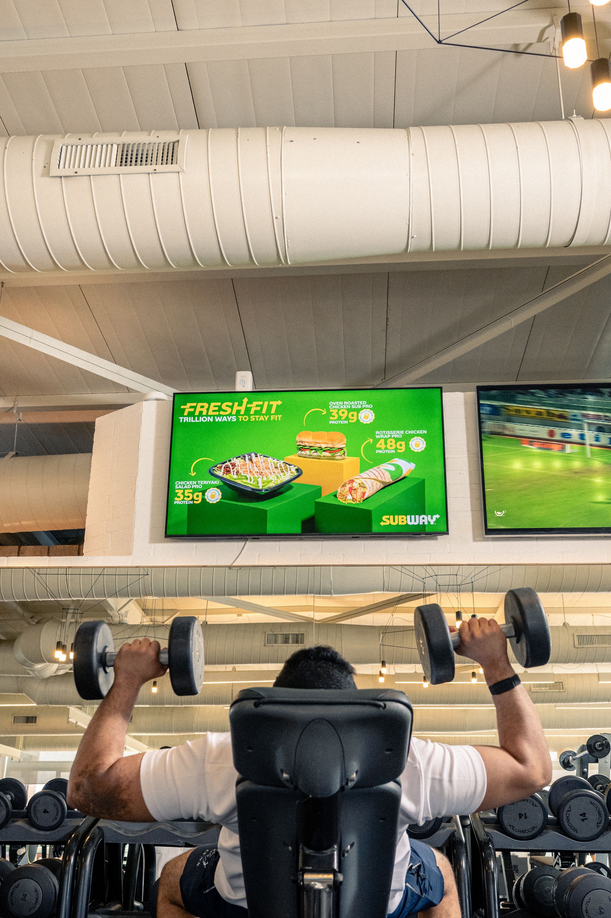 A meal ad on an Ad Space wall screen above a member training in a premium gym