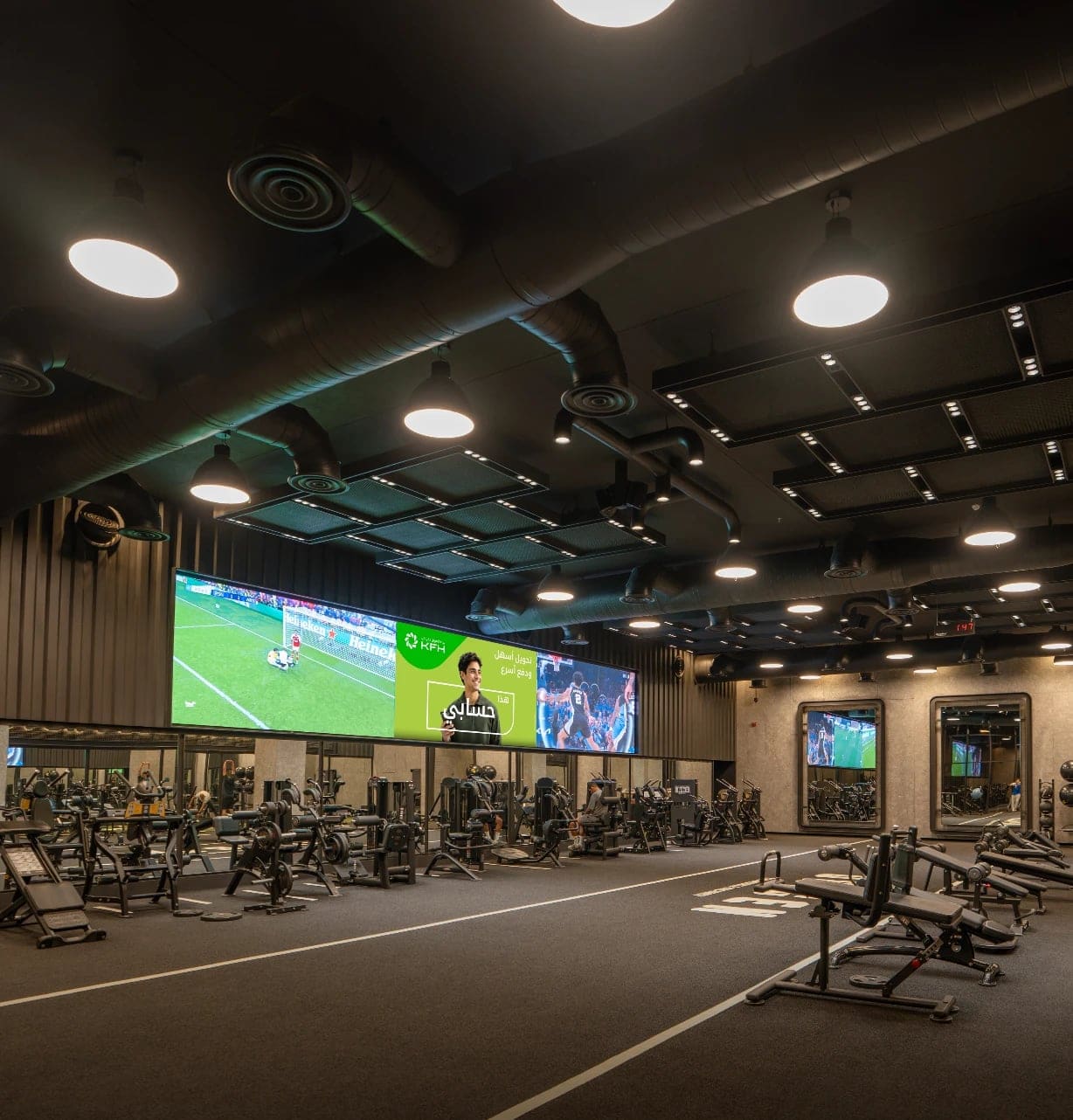 A bank ad on a long Ad Space video wall beside a football match, above the floor of a premium gym in Kuwait