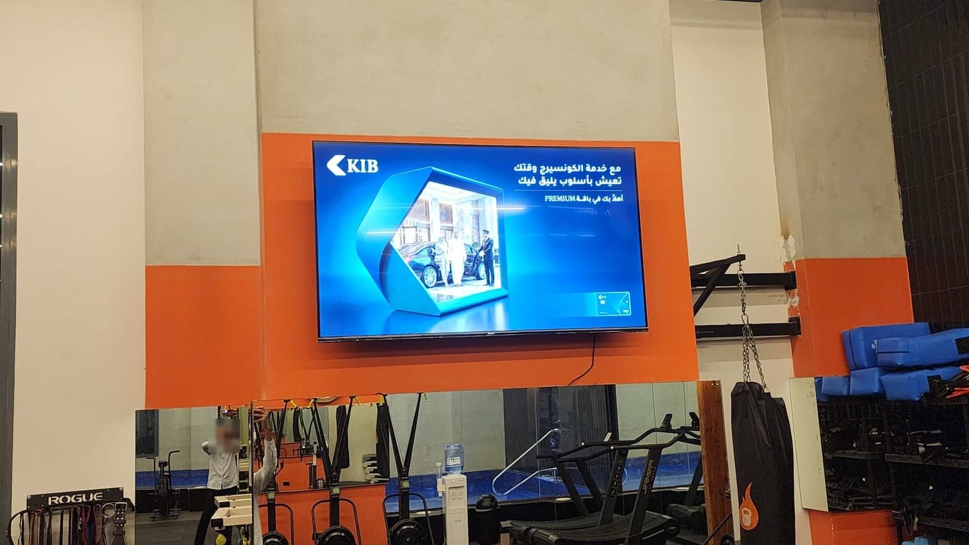 KIB's concierge ad on a wall screen on the orange wall of a gym, above the mirrors