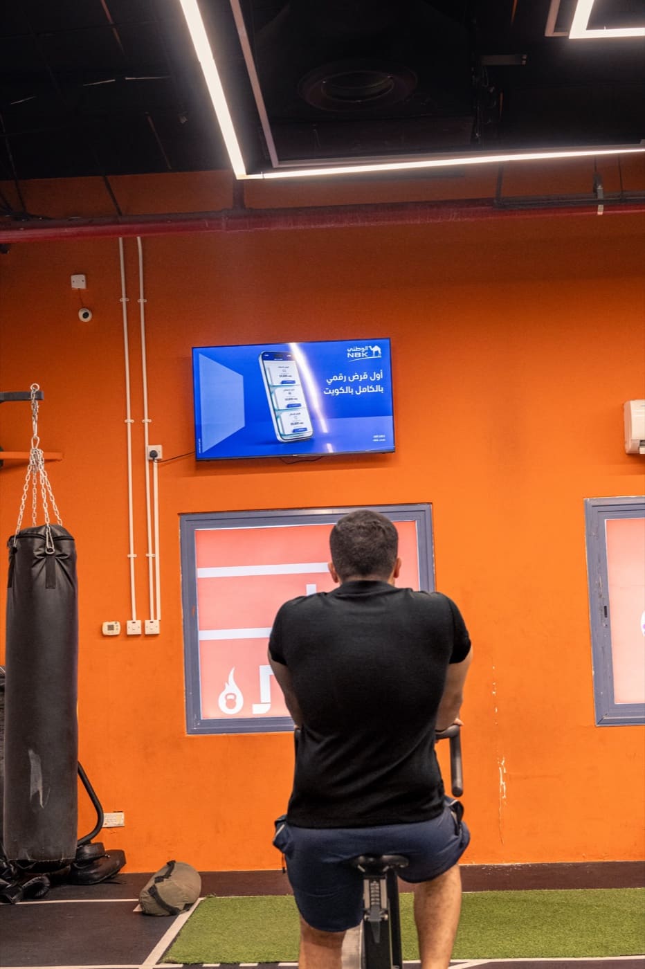 NBK's first digital loan ad on a wall screen on the orange feature wall of a premium men's gym