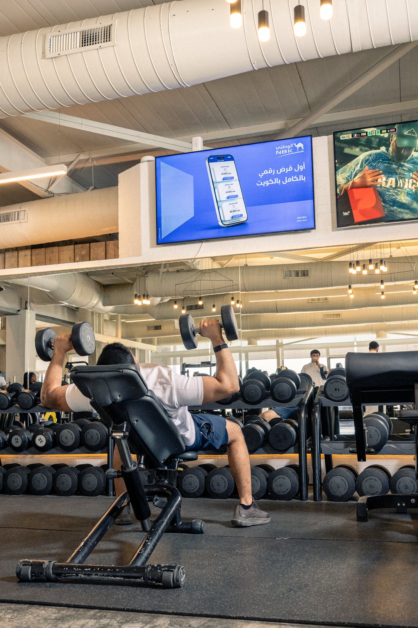 NBK's first digital loan ad on a large wall screen above the free weights of a premium gym