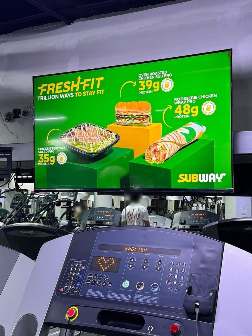 A Subway campaign on an Ad Space screen above a gym's treadmills